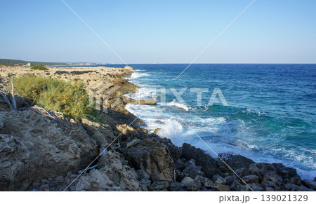 Waves crash against rugged cliffs on a sunny day along the beautiful coastline. 139021329