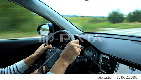 The driver hands lie on the steering wheel of a car at speed on a country road The driver hands lie on the steering wheel of a car at speed on a country road 139021689