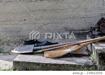 leaf rake, shovel, broom and garden shoes in front of a concrete wall. leaf rake, shovel, broom and garden shoes in front of a concrete wall. 139022030