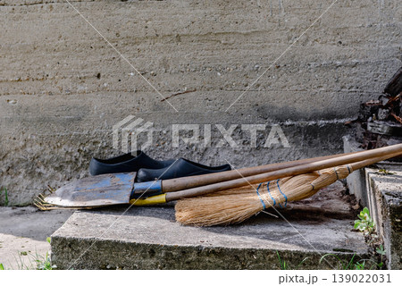 leaf rake, shovel, broom and garden shoes in front of a concrete wall. leaf rake, shovel, broom and garden shoes in front of a concrete wall. 139022031
