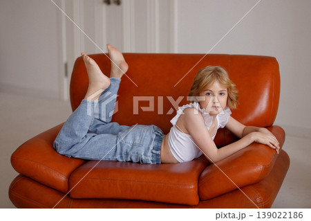 Relaxed child lying on orange leather sofa in bright modern living room Relaxed child lying on orange leather sofa in bright modern living room 139022186
