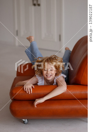 Relaxed child lying on orange leather sofa in bright modern living room Relaxed child lying on orange leather sofa in bright modern living room 139022187