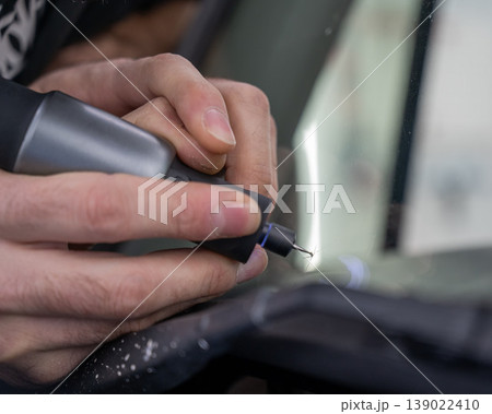A technician drills a hole during a car windshield chip repair. 139022410