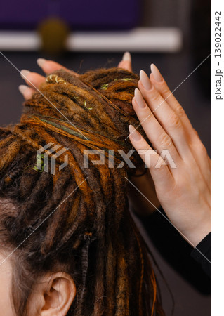 Hands braiding dreadlocks with decorative threads close up 139022442
