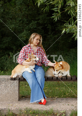 Woman With Dogs. Gentle Woman Enjoying Quiet Moment With Two Corgis In Lush Green Park Setting Woman With Dogs. Gentle Woman Enjoying Quiet Moment With Two Corgis In Lush Green Park Setting 139022445