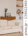 Beige plaid sofa standing in living room with white wall, wooden cabinet and flowers 139022460