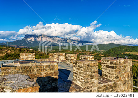 Ainsa Castle in the medieval village of Ainsa in Spain surrounded by stone walls with an elevated path leading to it. Ainsa Castle in the medieval village of Ainsa in Spain surrounded by stone walls with an elevated path leading to it. 139022491