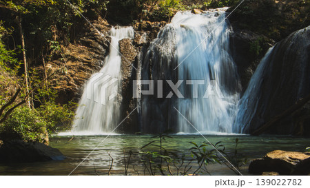 Multi-tier waterfall flowing into clear pool surrounded by lush tropical forest, scenic nature landscape and peaceful travel destination. Multi-tier waterfall flowing into clear pool surrounded by lush tropical forest, scenic nature landscape and peaceful travel destination. 139022782