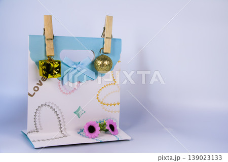 Decorative gift bag with ribbon, small golden ornaments and flowers isolated on white background. Still life concept for celebration, love, holiday decoration and gift packaging. 139023133