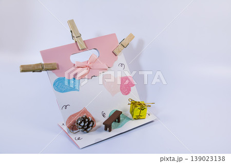 Decorative gift bag with heart pattern, ribbon, small present and pine cone on soft background. Romantic celebration concept with copy space for design or greeting. Decorative gift bag with heart pattern, ribbon, small present and pine cone on soft background. Romantic celebration concept with copy space for design or greeting. 139023138