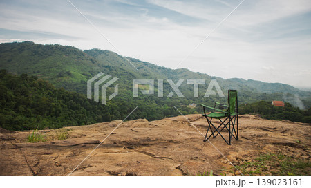 Camping chair on rocky mountain viewpoint overlooking green hills and forest valley. Scenic outdoor travel scene symbolizing freedom, adventure, relaxation and peaceful nature escape. 139023161