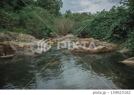 Clear freshwater stream flowing through natural rock formations in lush green forest. Peaceful tropical landscape symbolizing purity, environment, wilderness and untouched nature. Clear freshwater stream flowing through natural rock formations in lush green forest. Peaceful tropical landscape symbolizing purity, environment, wilderness and untouched nature. 139023162