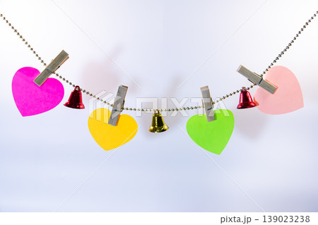 Colorful heart shaped paper notes hanging on string with small bells and clothespins isolated on white background. Romantic decoration template with copy space for love message. Colorful heart shaped paper notes hanging on string with small bells and clothespins isolated on white background. Romantic decoration template with copy space for love message. 139023238