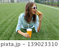 Happy young woman eating burger fast food drinking juice, teenage girl lying in summer park 139023310