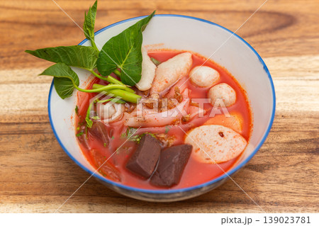 Yentafo Thai pink noodle soup with seafood fish balls blood tofu and morning glory in rich red broth served in bowl on wooden table 139023781