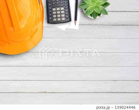 Orange safety helmet or hard hat,coffee,calculator and construction paper plans on wood table background. Orange safety helmet or hard hat,coffee,calculator and construction paper plans on wood table background. 139024446