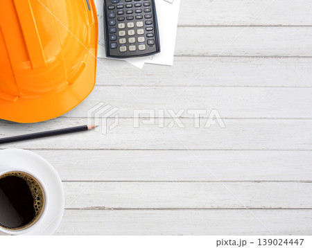 Orange safety helmet or hard hat,coffee,calculator and construction paper plans on wood table background. Orange safety helmet or hard hat,coffee,calculator and construction paper plans on wood table background. 139024447