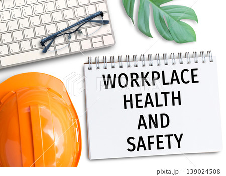 Orange safety helmet with words workplace health and safety write in notebook. Orange safety helmet with words workplace health and safety write in notebook. 139024508