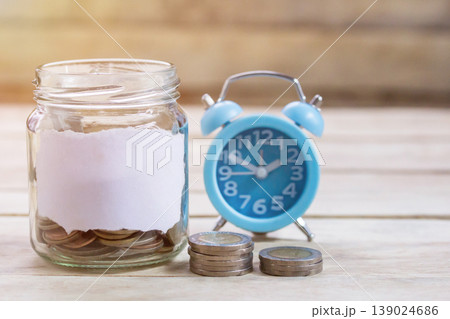Coins,alram clock and pencil with empty notebook on wood table background. 139024686