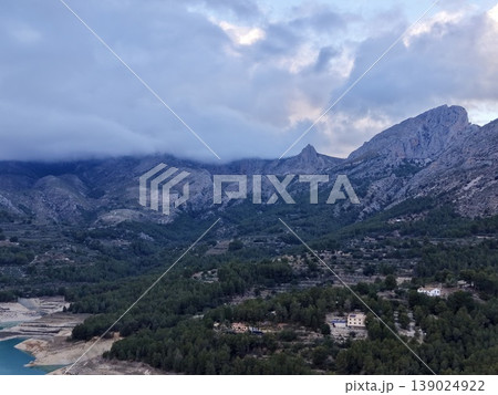 Dramatic Cloudy Sky Over Rugged Village, Misty Mountain Pass With Pine Dwellings Under Dark Skies Dramatic Cloudy Sky Over Rugged Village, Misty Mountain Pass With Pine Dwellings Under Dark Skies 139024922