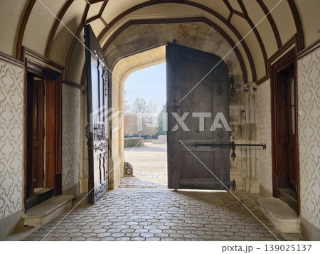 Stone Hallway With Open Gate And Morning Glow. Old Vaulted Corridor With Oak Door And Cobblestone Floor Stone Hallway With Open Gate And Morning Glow. Old Vaulted Corridor With Oak Door And Cobblestone Floor 139025137