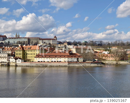 Bright Scenic Vista. Beautiful View Of Vibrant Town Along River With Castle Silhouette And Fluffy Clouds Bright Scenic Vista. Beautiful View Of Vibrant Town Along River With Castle Silhouette And Fluffy Clouds 139025167