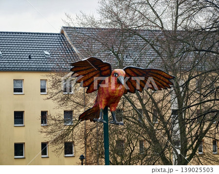 Lively Metal Parrot Figure With Extended Wings High Above Urban Courtyard During Overcast Winter Days Lively Metal Parrot Figure With Extended Wings High Above Urban Courtyard During Overcast Winter Days 139025503