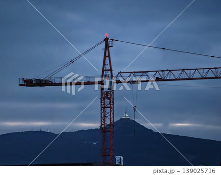 Evening Industrial Construction Scene. Silhouette Of Crane Against Evening Mountain Background Evening Industrial Construction Scene. Silhouette Of Crane Against Evening Mountain Background 139025716