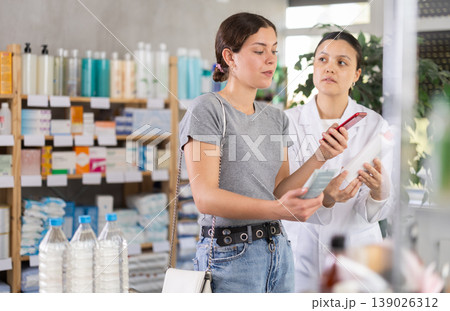 Young girl scanning QR on cream while pharmacist offering in drugstore Young girl scanning QR on cream while pharmacist offering in drugstore 139026312