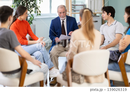 Youth girls and guys sit at circle, listen to senior man coach. Youth girls and guys sit at circle, listen to senior man coach. 139026319