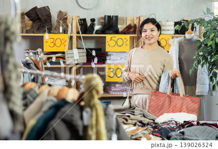 Latin girl is busy looking at clothes items in store, she chooses jeans Latin girl is busy looking at clothes items in store, she chooses jeans 139026324