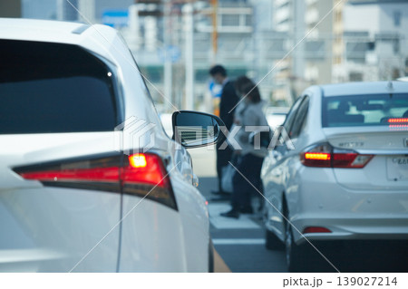 都市の交差点で信号待ちの車の列と横断歩道を渡る人々の姿	 139027214