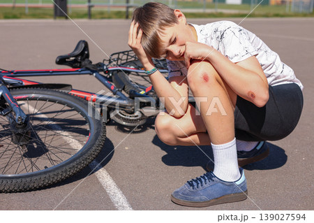 Boy with knee injury after bicycle accident sitting on asphalt road with fallen bike Boy with knee injury after bicycle accident sitting on asphalt road with fallen bike 139027594