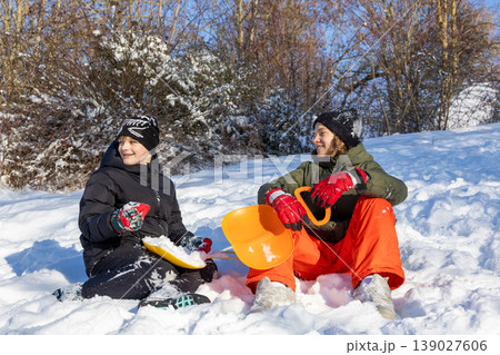Children resting in snow with sleds winter outdoor leisure friendship lifestyle scene 139027606
