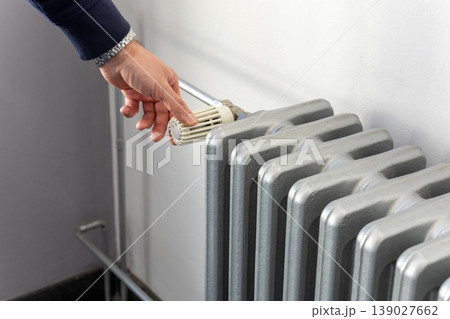 Person turning radiator thermostat valve side view heating system regulation indoors Person turning radiator thermostat valve side view heating system regulation indoors 139027662