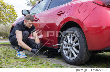 Man replacing car wheel with jack and tools on roadside during tire change process Man replacing car wheel with jack and tools on roadside during tire change process 139027696
