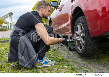 Man changing car tire with jack and wrench on roadside pavement in daylight Man changing car tire with jack and wrench on roadside pavement in daylight 139027750