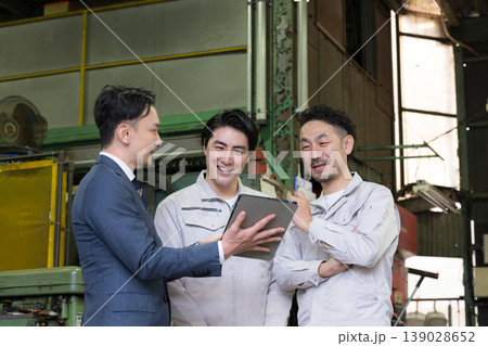 工場でタブレットを使い3人で打ち合わせする作業員とビジネスマンの現場、dxやIT、AI化の機械の導入 139028652