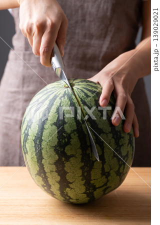 Woman's hands holding a knife and preparing to slice a fresh watermelon on a wooden cutting board 139029021