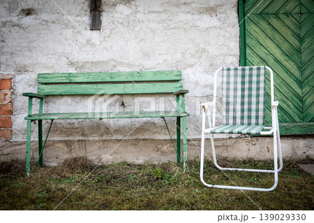 Green Wooden Bench and Checkered Chair Against Rustic Wall 139029330