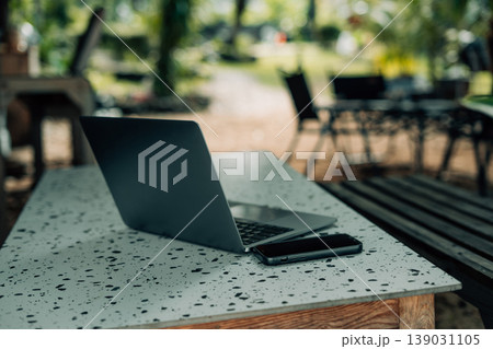 Laptop computer and smartphone placed on a table in a relaxed outdoor tropical cafe setting. 139031105