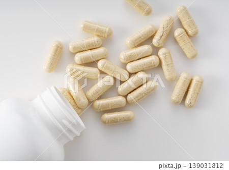 白いボトルからこぼれ落ちるハーブサプリメントのカプセル、健康食品や漢方のイメージ素材(真上) 白いボトルからこぼれ落ちるハーブサプリメントのカプセル、健康食品や漢方のイメージ素材(真上) 139031812