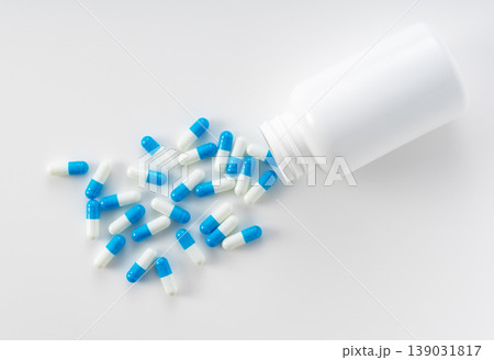 白いボトルからこぼれ出る青と白のカプセル剤、白背景の俯瞰イメージ素材 139031817
