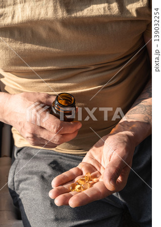 Mans hands holding a handful of fish oil capsules poured from a brown bottle, promoting daily health and wellness. Healthy lifestyle, self-care Mans hands holding a handful of fish oil capsules poured from a brown bottle, promoting daily health and wellness. Healthy lifestyle, self-care 139032254