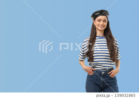 Woman smiles and poses with hands in pockets against blue wall Woman smiles and poses with hands in pockets against blue wall 139032865