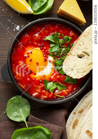 Dish features egg in red sauce with bread and vegetables 139033056