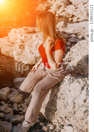 Woman sitting coast relaxing on rocky shoreline during golden sunset light outdoors at sea 139033121