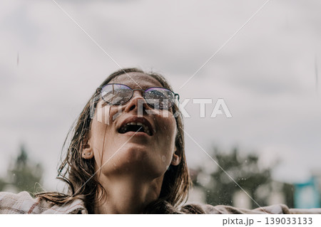 Woman rain glasses looking up at the sky with a wet face during a summer storm feeling refreshed and free 139033133