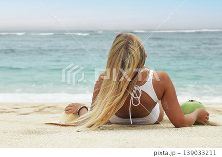 Woman enjoys the beach while holding a coconut Woman enjoys the beach while holding a coconut 139033211