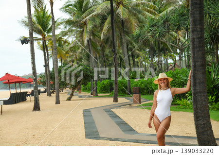 Woman walks along a sandy path near palm trees Woman walks along a sandy path near palm trees 139033220